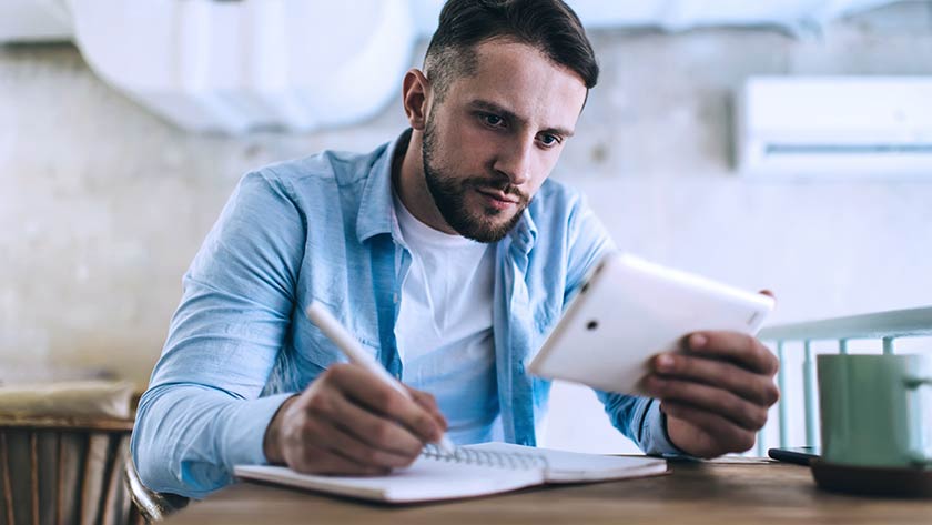 Man writing notes looking at mobile phone