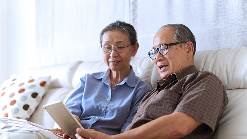 older-couple-sitting-on-sofa-reviewing-tablet