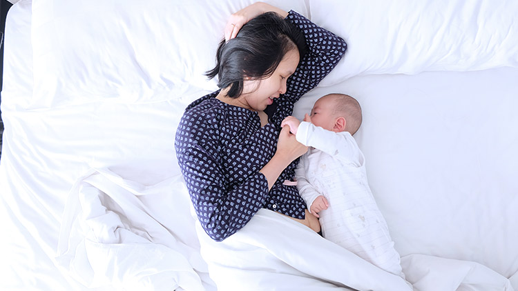 Woman side lying in bed with infant baby