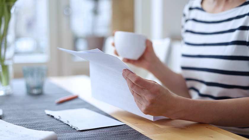 Woman at home drinking coffee and looking over letter
