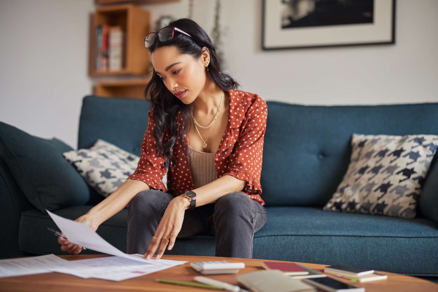 A woman sits on a blue couch and sifts through paperwork on a coffee table. Learn which business expenses vs. personal expenses are deductible.