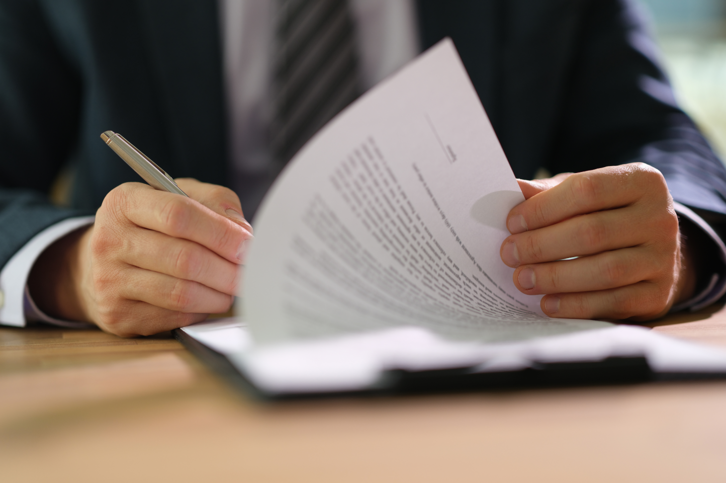 A person seated at a desk signs a durable power of attorney form on a clipboard. 