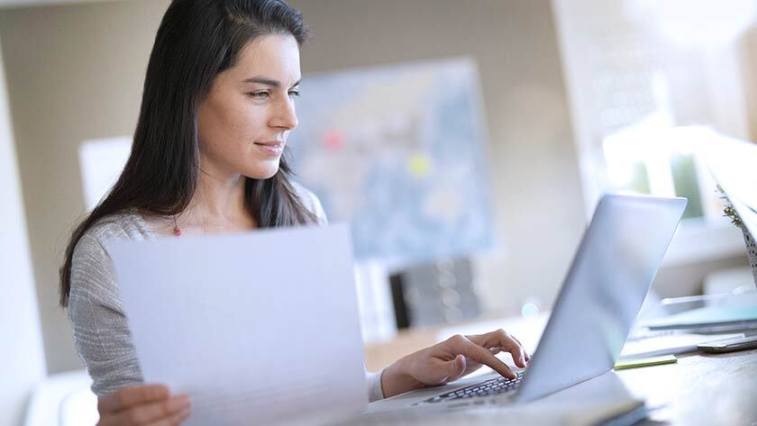 woman looking at paperwork working on laptop