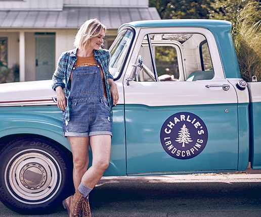 A smiling business woman stands next to a truck with her company logo on the door.