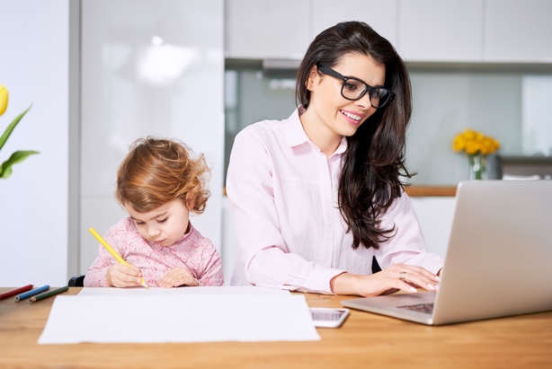 A mom works on her laptop while her daughter draws beside her.