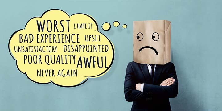 Person in suit wearing a paper bag with a drawn-on sad face over his head with a thought bubble filled with negative phrases