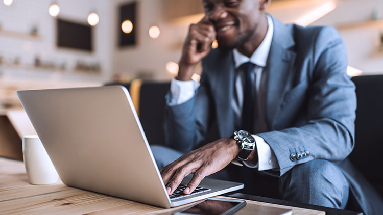 Business man on phone smiling and typing on laptop