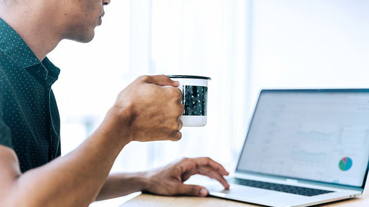 Man looks at computer and drinks coffee