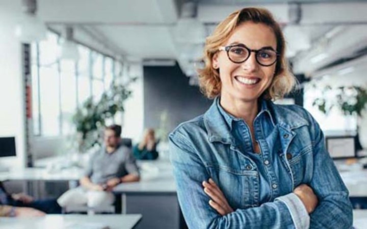 Woman in denim button down shirt proudly crossing arms and smiling in office