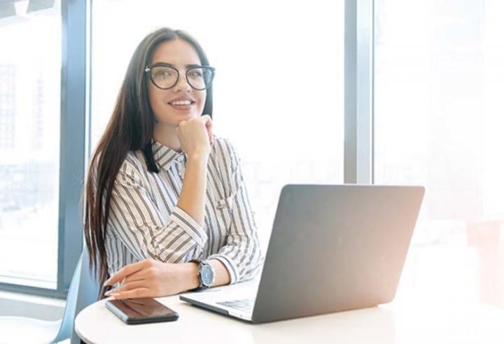 Smiling woman resting chin on hand sitting at table with open laptop