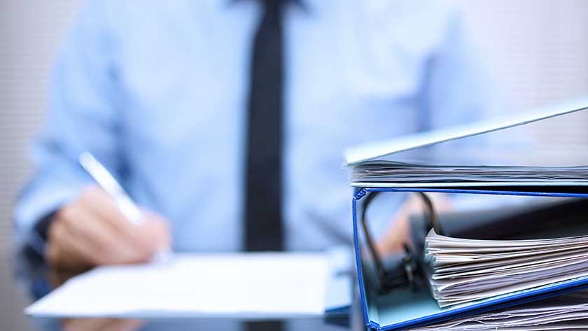 businessman-writing-on-paper-next-to-binder