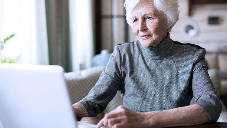 elderly woman looking at laptop in grey shirt 