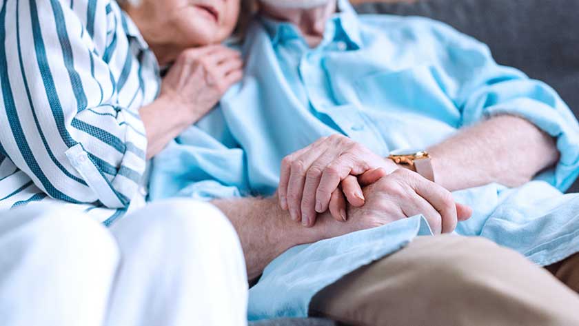 Elderly woman and man sit on sofa and hold hands