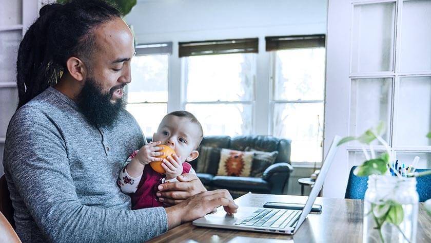 man-holding-baby-working-from-home wearing grey shirt