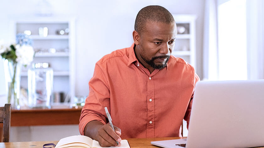 man-taking-notes-serious-looking-at-laptop