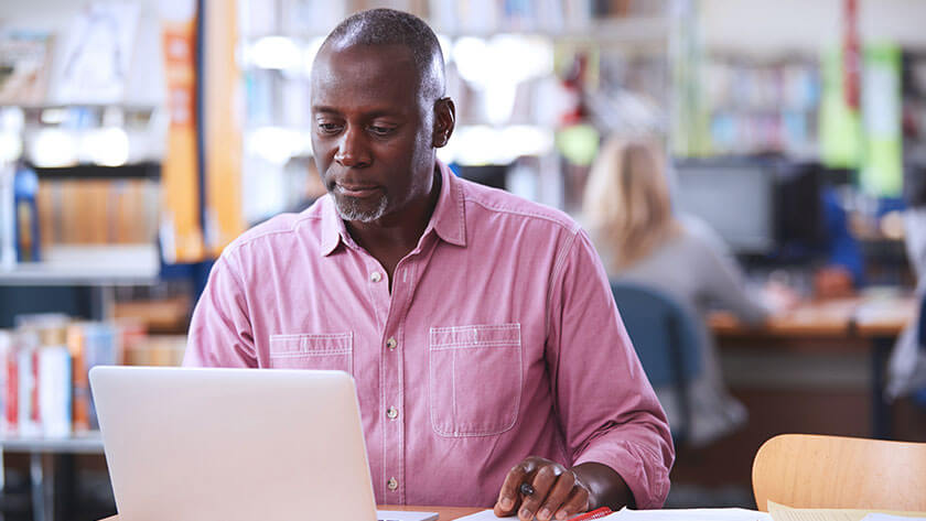 older-man-typing-on-laptop-taking-notes