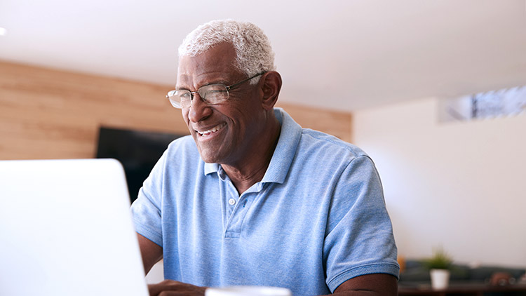 Senior man looks at laptop smiling