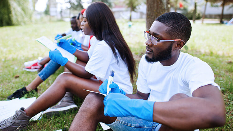 volunteers-with-clipboards-in-park sitting in the grass 