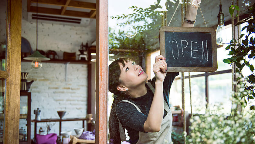 woman opening her store hanging open sign
