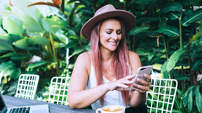 woman-smiling-scrolling-on-phone-outside at a cafe