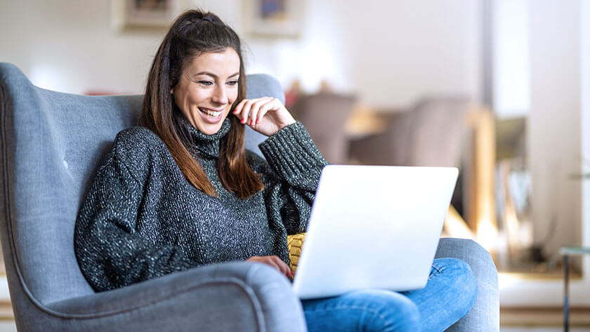 woman-smiling-sitting-in-chair-at-home-on-laptop working from home 