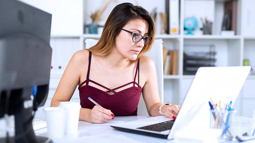 woman taking notes looking at computer