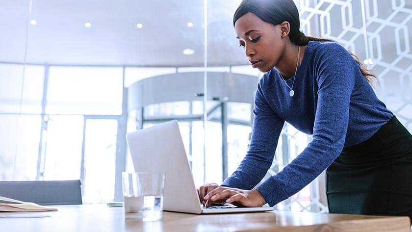 woman-typing-on-laptop-in-office-by-windows wearing blue sweater 