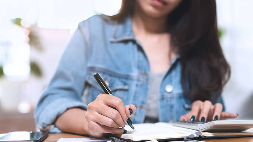 woman-wearing-jean-jacket-writing-and-calculating at her desk
