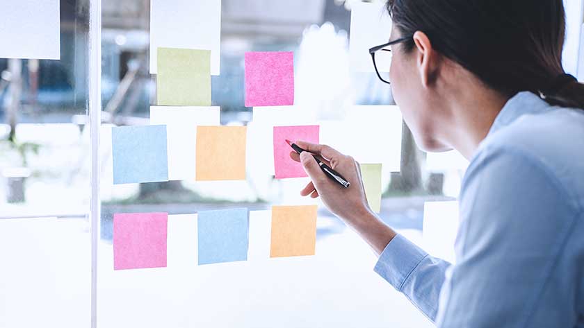 woman-writing-with-post-it-notes-posting-on-glass 1