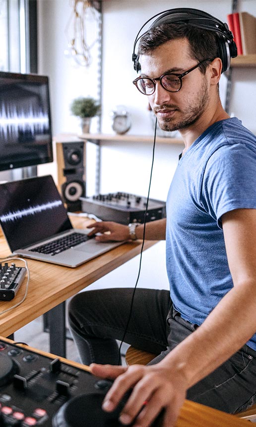 Man with glasses using a DJ setup to make music.