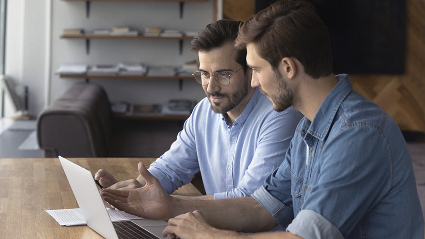 2 men in denim shirts looking at a laptop and talking 