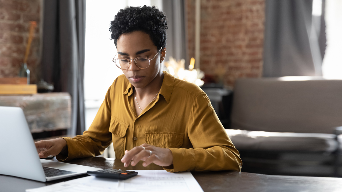 A woman uses a calculator while using a laptop computer. Businesses can repay employees for business expenses using either an accountable plan or a non-accountable plan.