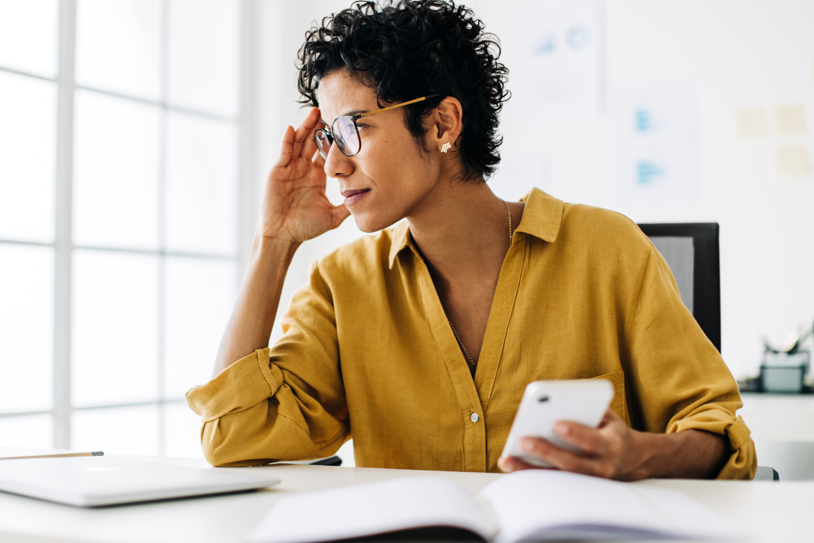 A woman seated at a desk holds her temples and looks to the side through a window as she holds a cell phone. Before you start business during a recession, consider the avoiding the riskiest kind of business.   