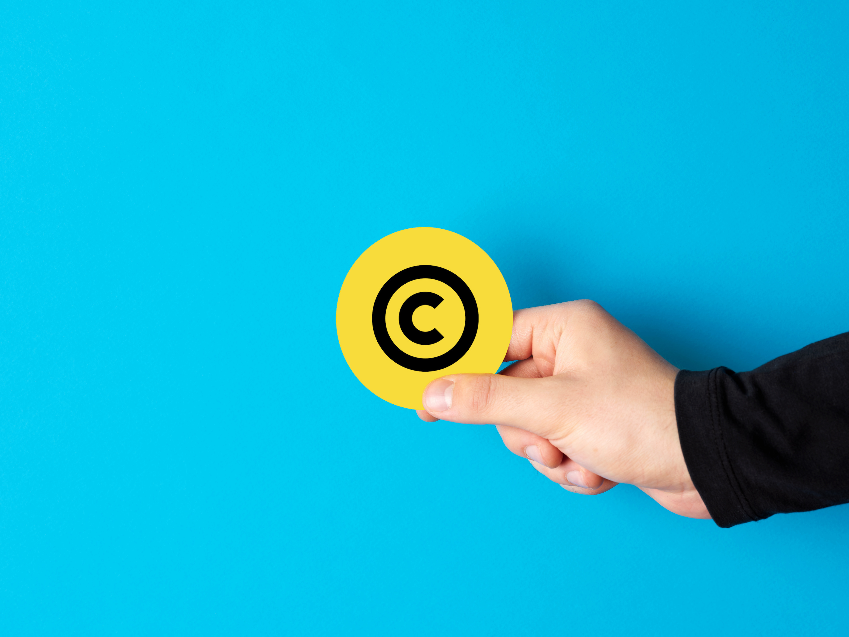 A hand reaches out, holding a yellow circle with the copyright sign.