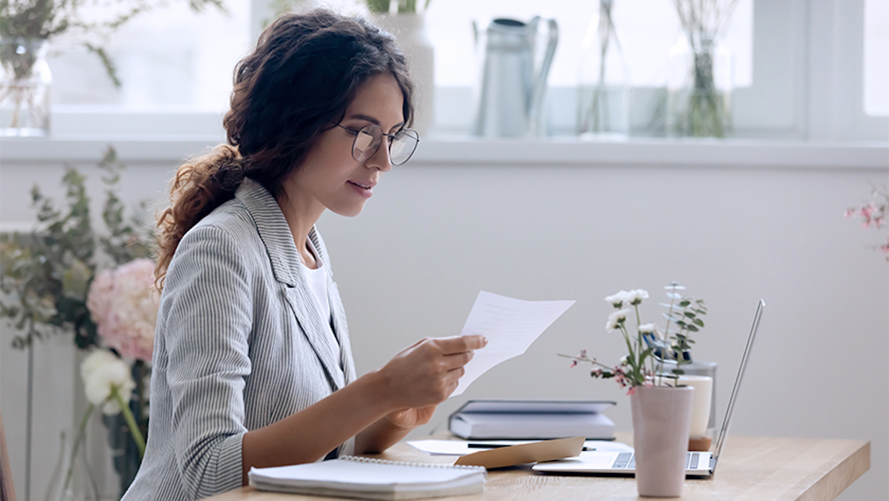 A woman seated at a desk reads her living trust form. Using an online service like LegalZoom can help lower some of the costs associated with setting up a living trust..