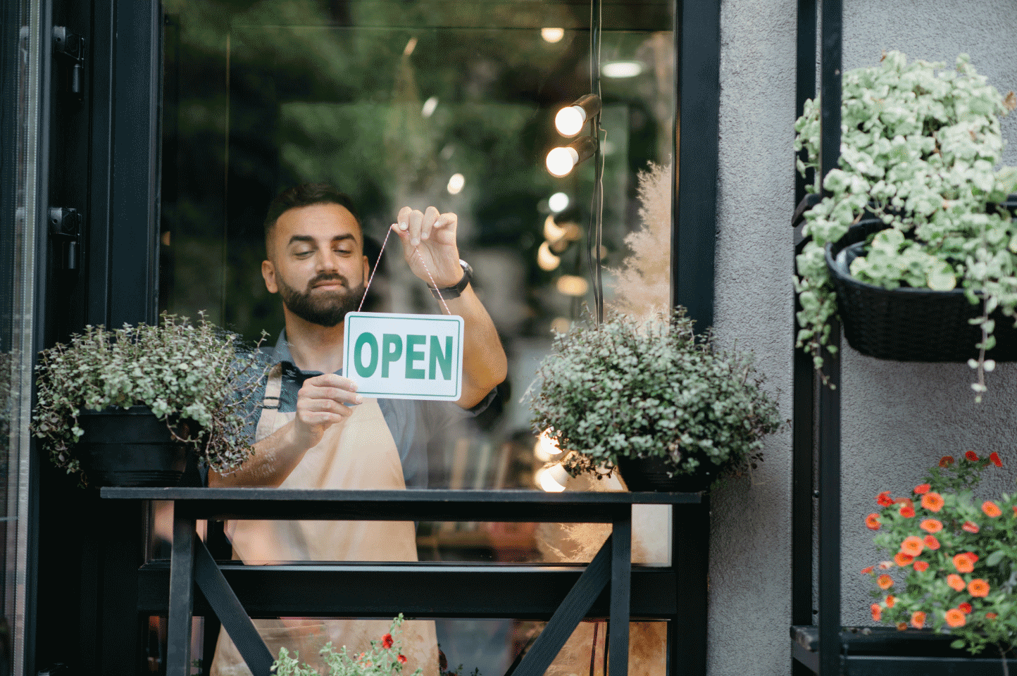 A man turns a sign from "closed" to "open" in the window of a shop that has many plants on its exterior. Learn why you may not need a physical address if you have a virtual business.