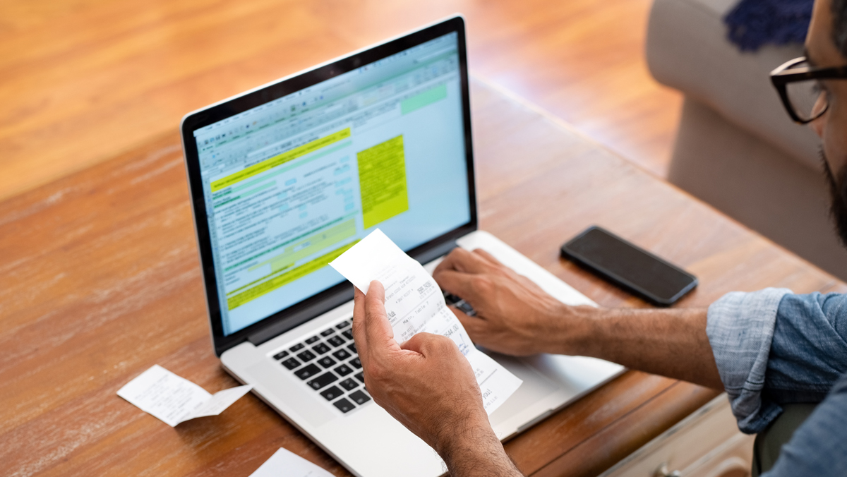 A man checks a receipt against information his laptop computer while calculating his expense reimbursement.