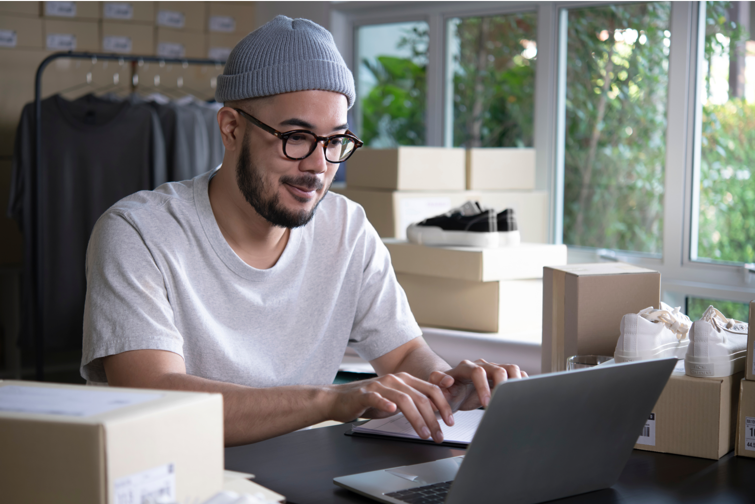 A man sits at a table typing on his open laptop computer while reading about U.S. Post Office Informed Delivery. 