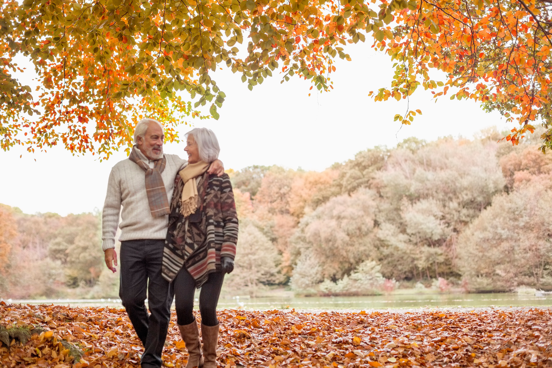 A man with his arm around a woman talks about his estate planning wishes as they walk among trees.