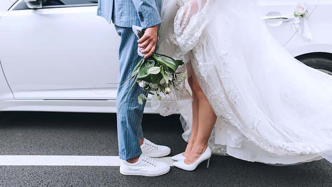 A bride and groom stand in front of their limo. Prenups are a practical tool that benefits married couples from all walks of life.