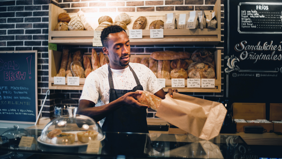 A man puts a baguette into a paper wrapper. His business may be eligible for tax cuts under the TCJA.