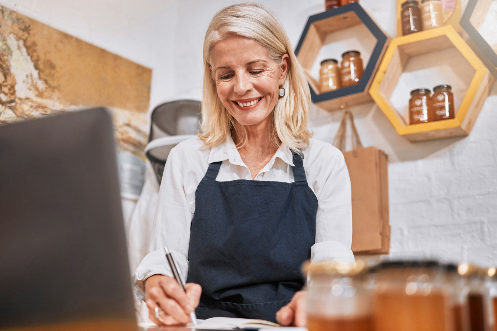 The owner of a small business stands behind the counter at her shop and takes notes in a notebook..