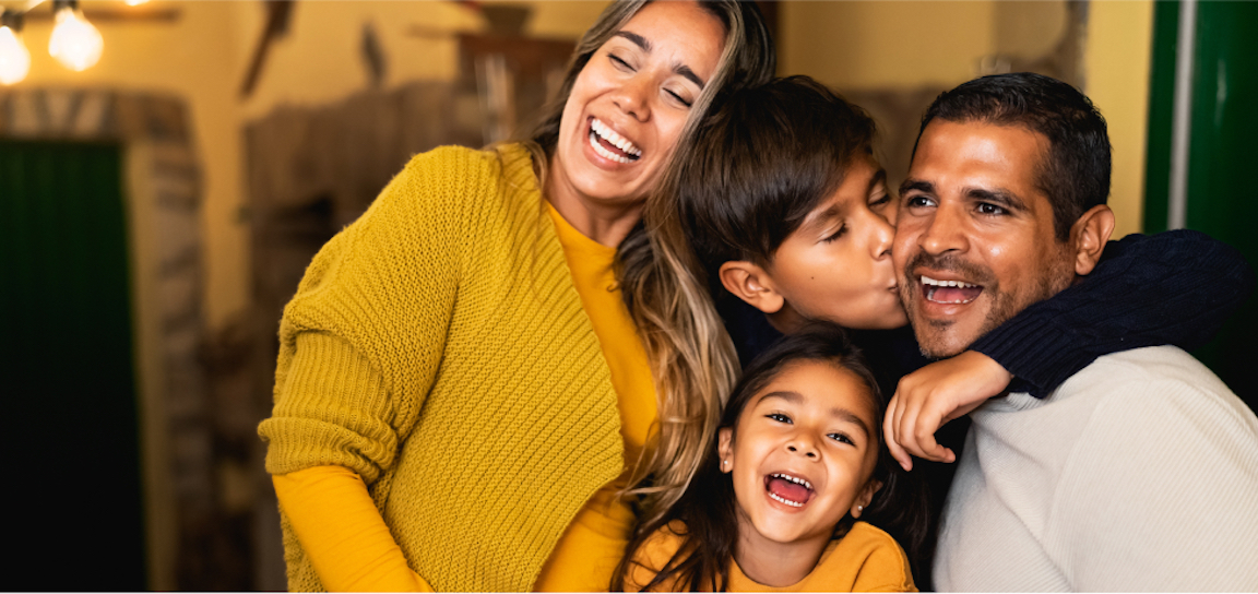 A woman, man, and their two children smile and embrace one another. To safeguard your family after your death, consider transferring assets into a living trust.