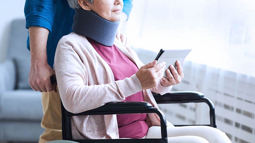 A woman in a wheelchair reads an iPad as a nurse stands behind her guiding the chair. Make sure to keep your living trust current and effective, responding to life events and changing circumstances.