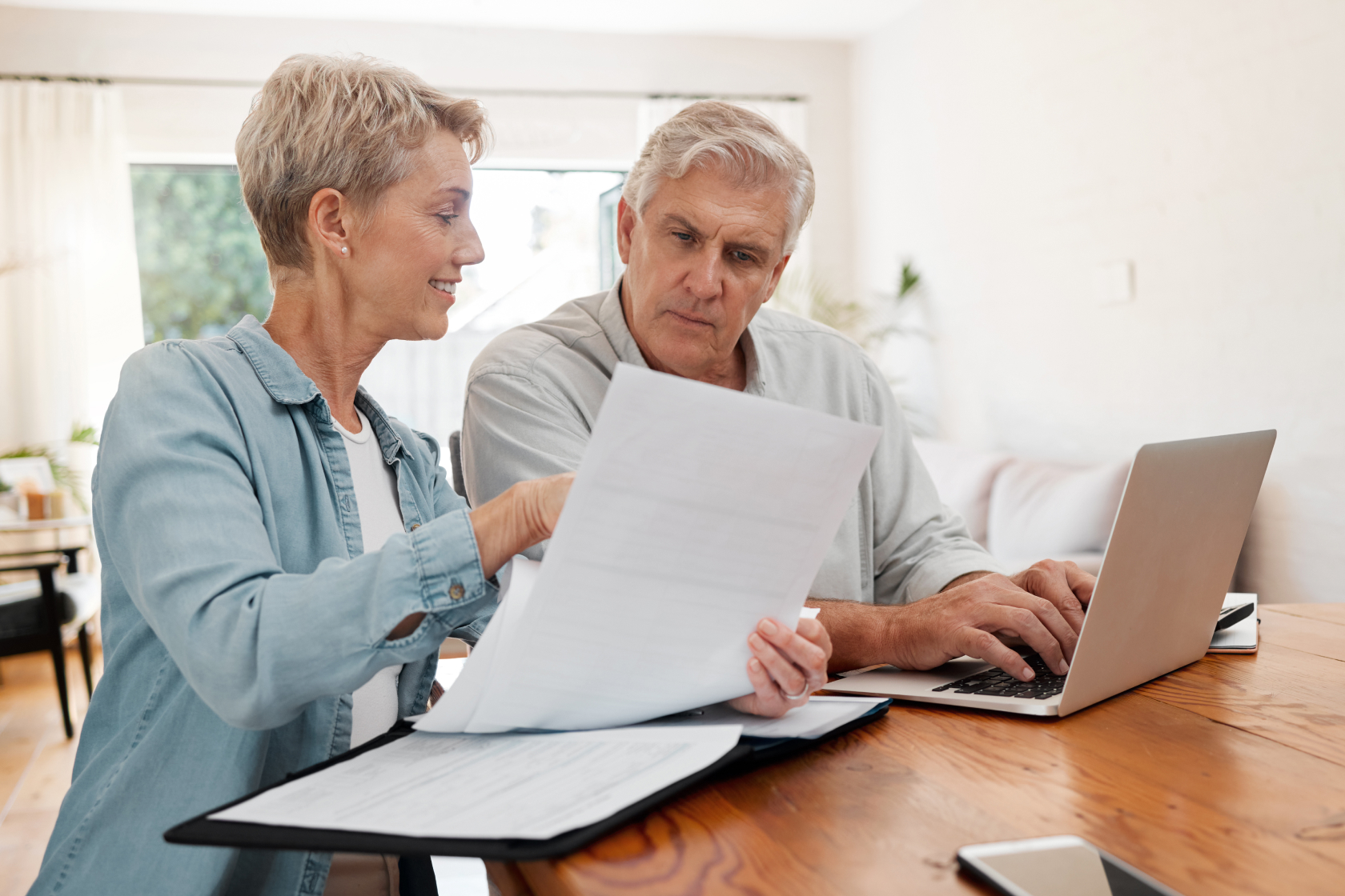 A woman holding documents and a man typing on an open laptop go over their letter of testamentary. 