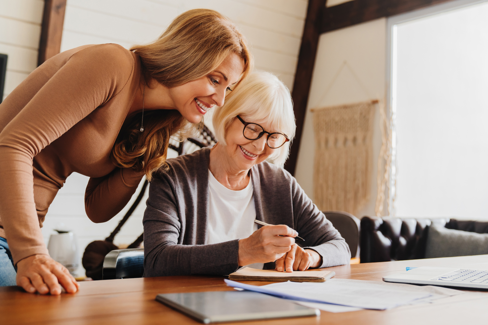 A woman leans over an elderly woman seated at a table signing documents related to inheritance taxes. An inheritance tax  is a levy beneficiaries pay when they inherit assets.