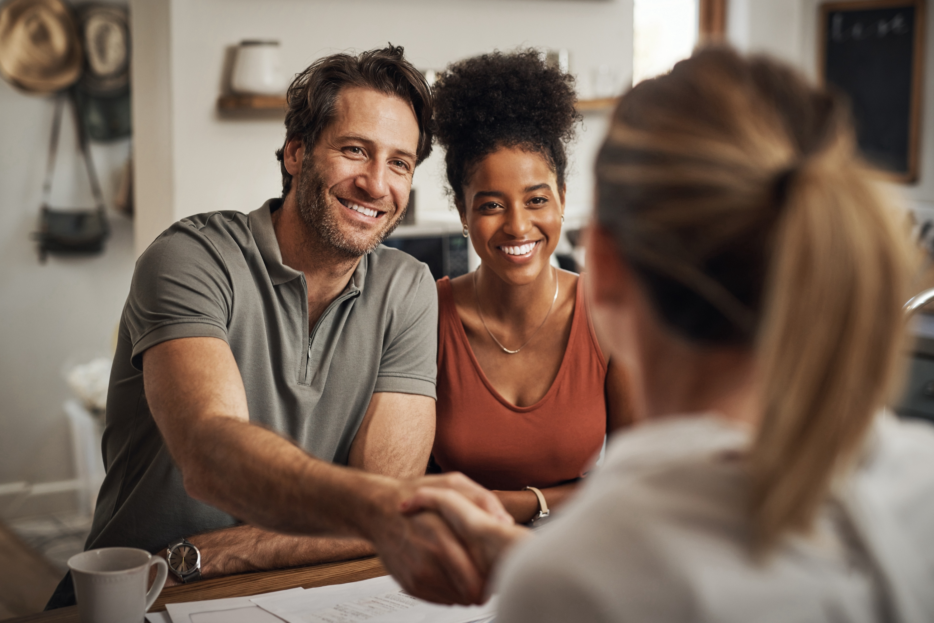 A man shakes hands with a woman seated across a desk from him as another woman, seated next to the man, looks on and smiles. They have just completed their paperwork for their wills.