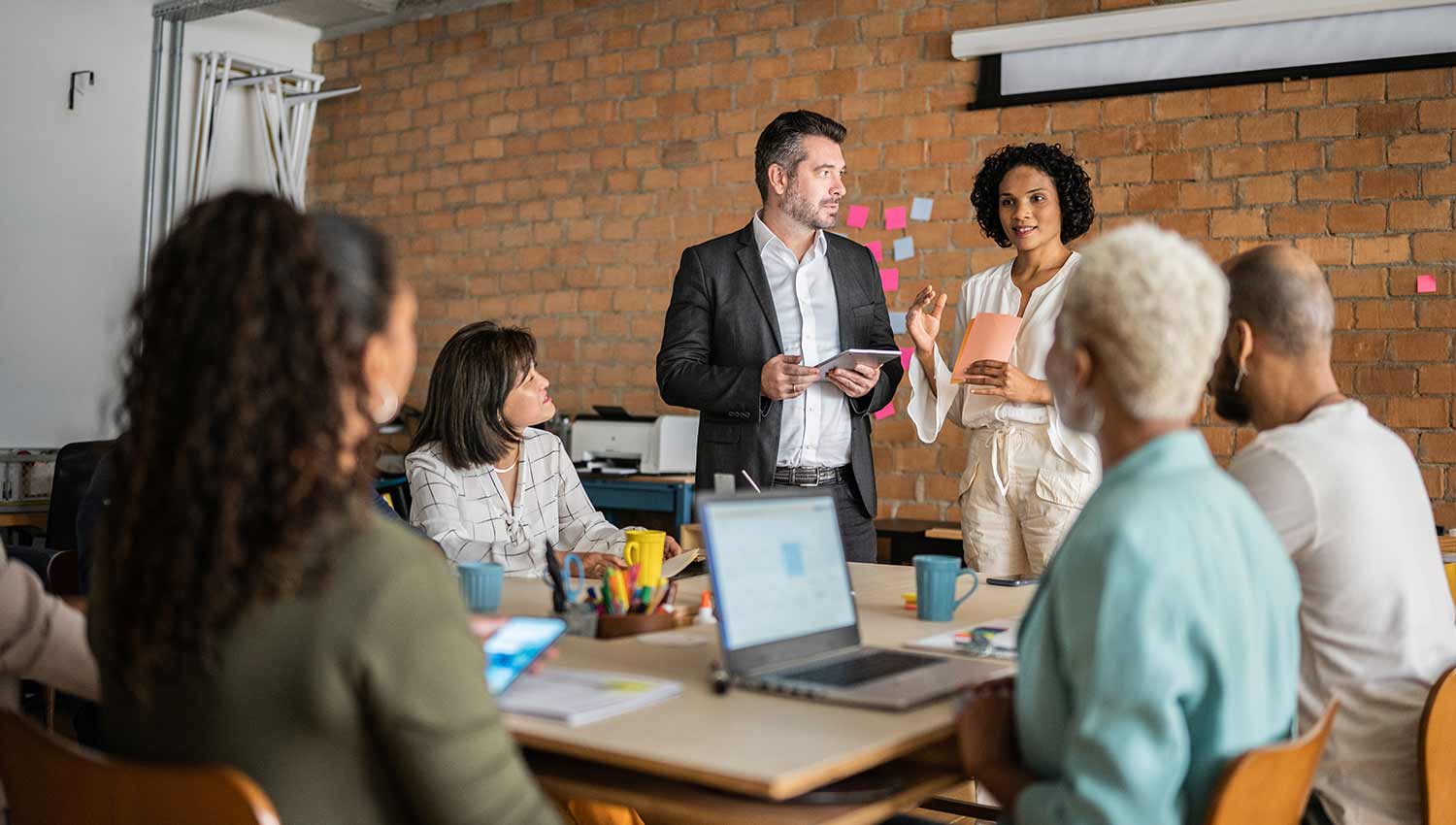 Two people stand while making a presentation to a group of four people seated around a table. Learn how to file an annual report for your LLC.