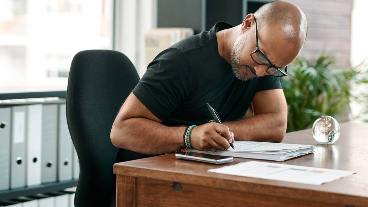 A man seated at a desk writes in a notebook while considering the elements of intellectual property assignment.