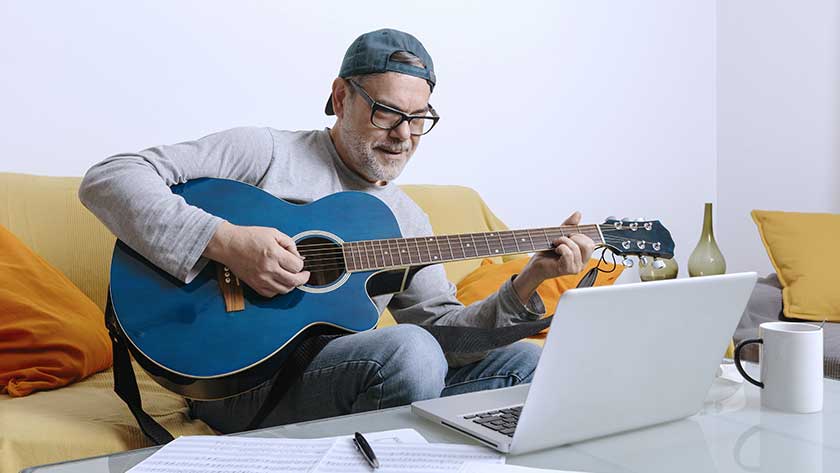 main-playing-guitar-looking-at-laptop-on-sofa